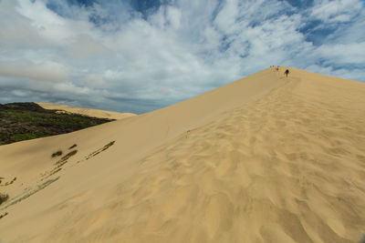 View of sand dunes in desert against cloudy sky