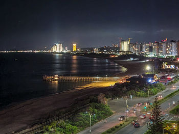 Illuminated city by river against sky at night