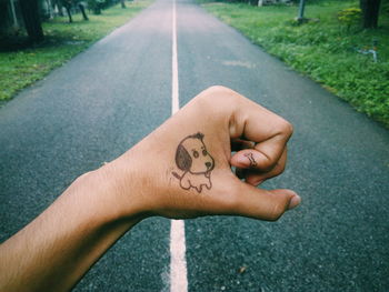 Cropped image of hand with dog sketch against empty road
