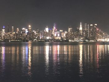 Illuminated buildings by sea against sky at night