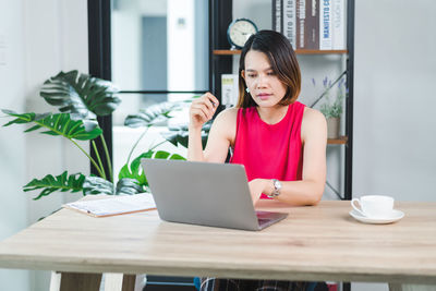 Young woman using mobile phone while sitting on table