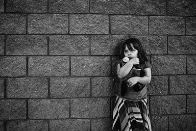 Girl holding toy while standing against wall