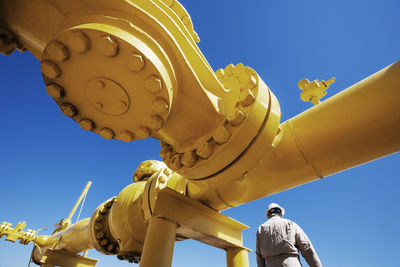 Male worker standing below yellow painted pipeline at oil refinery