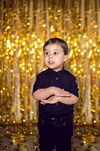 Boy in black clothes at christmas standing in a room on a background of gold tinsel on the wall