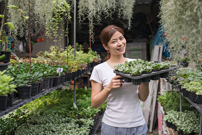 Portrait of smiling woman holding plants in greenhouse