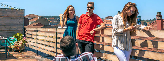 Happy friends talking in rooftop city while woman looking her phone