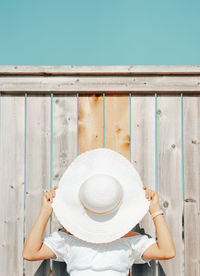 Young woman covering face with hat against wooden wall outdoors