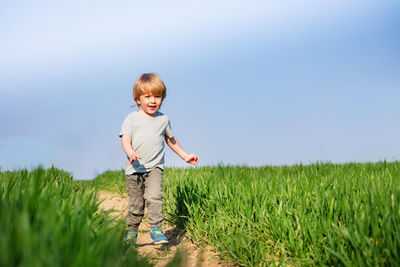 Side view of boy standing on field against clear sky