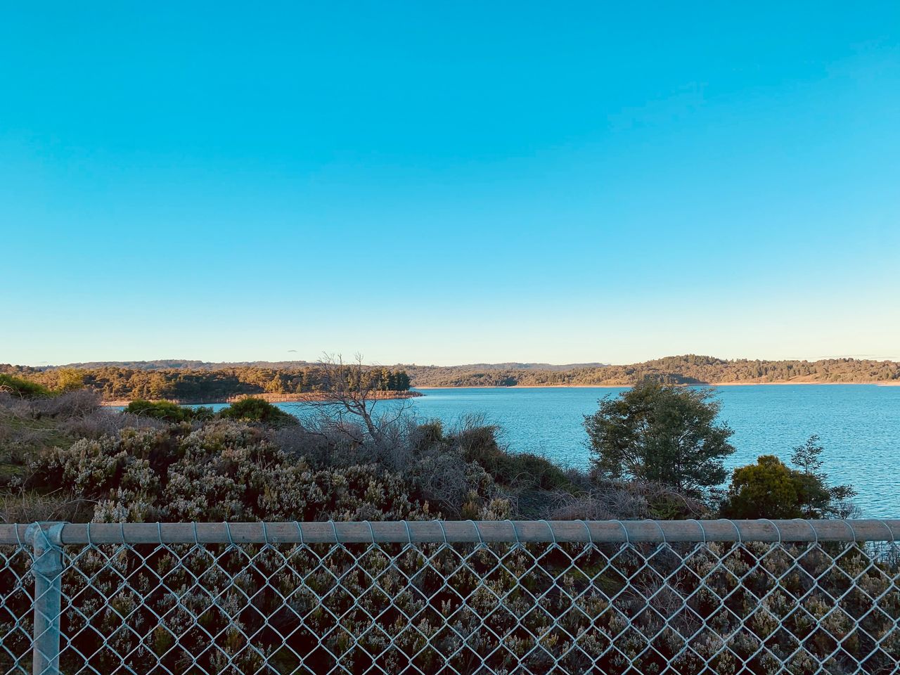 sky, sea, fence, nature, horizon, water, blue, clear sky, coast, no people, scenics - nature, morning, reflection, landscape, tranquility, tranquil scene, shore, security, mountain, land, environment, day, copy space, plant, beauty in nature, tree, dusk, protection, outdoors, sunlight, ocean, cloud, chainlink fence, wire