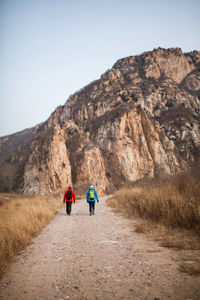 Rear view of people walking on mountain road against clear sky