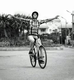 Full length of man riding bicycle with arms outstretched on road against clear sky