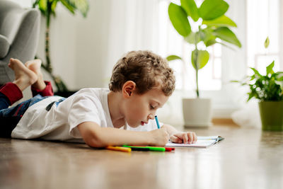 A little boy draws, lying on the floor, having fun. happy childhood, positive emotions. side view