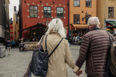 Rear view of senior couple holding hands while walking together in city