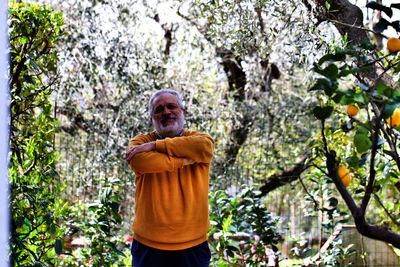 Man standing with arms crossed amidst lemon trees