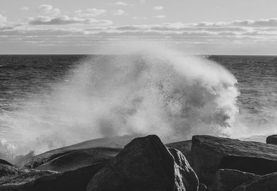 Waves splashing on rocks against sky