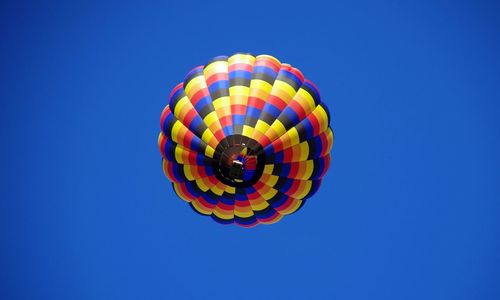Low angle view of multi colored balloons against clear blue sky