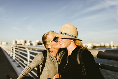 Loving mother kissing daughter on pier against sky in city