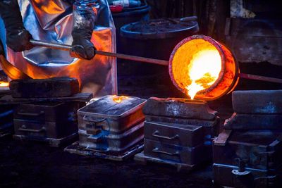 Midsection of worker pouring cast iron in container at still mill