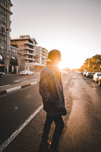 Man on city street against sky during sunset