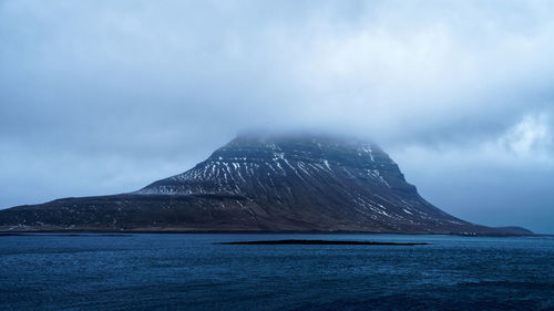 Scenic view of sea by mountain against sky