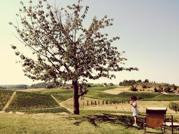 Girl standing on field by tree against clear sky