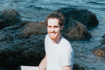 Portrait of man sitting on rock by sea