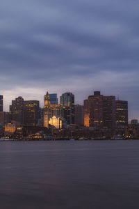 Sea by buildings against sky at dusk