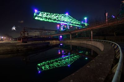 Illuminated bridge over river in city against sky at night