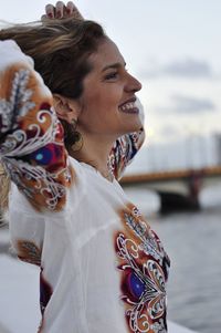 Side view of smiling woman looking away while standing against sky