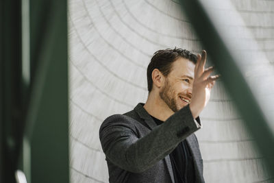 Smiling male entrepreneur waving hand while standing in convention center looking away