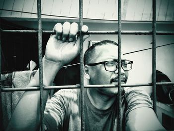 Man wearing eyeglasses while looking through metallic fence