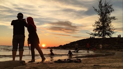 Silhouette people standing on beach against sky during sunset