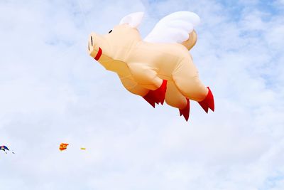 Low angle view of inflatable pig toy flying against sky