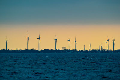 Scenic view of windmills and lake against sky during sunset 