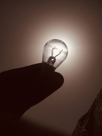 Close-up of hand holding light bulb against sky