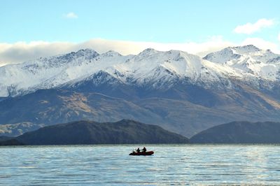 People in boat on lake against snow covered mountains and sky