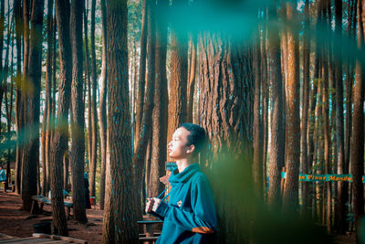 Side view of man standing by tree trunk in forest