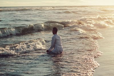 Man sitting in sea during sunset