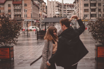 Man photographing woman standing against buildings in city