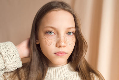 Beautiful teenage girl with golden freckles on face posing on beige background