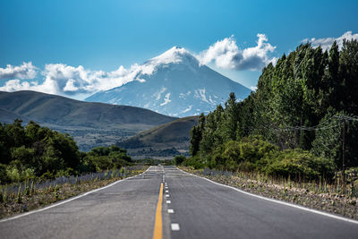 Empty road along trees and mountains against sky