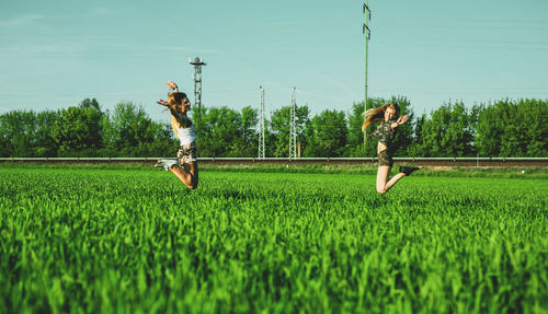 Friends jumping on grassy field against sky