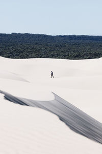 Distant view of man walking on sand during sunny day