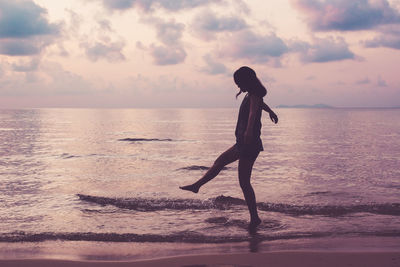 Side view of woman on shore at beach against sky during sunset