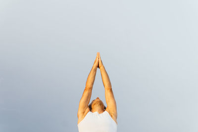 Cropped man in activewear raising arms against gray sky while doing yoga in daytime