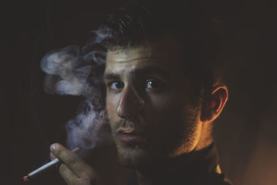 Close-up portrait of man smoking against black background