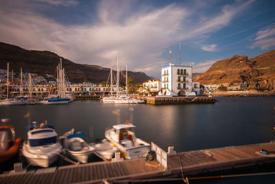 Boats moored in harbor by buildings against sky