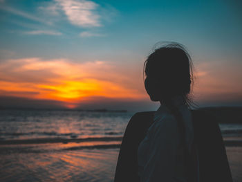 Rear view of woman standing at beach against sky during sunset