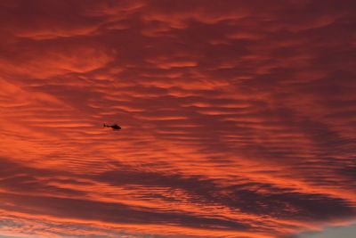 Low angle view of silhouette helicopter flying against dramatic sky