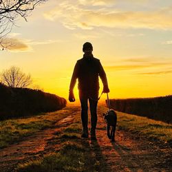 Man with dog against sky during sunset